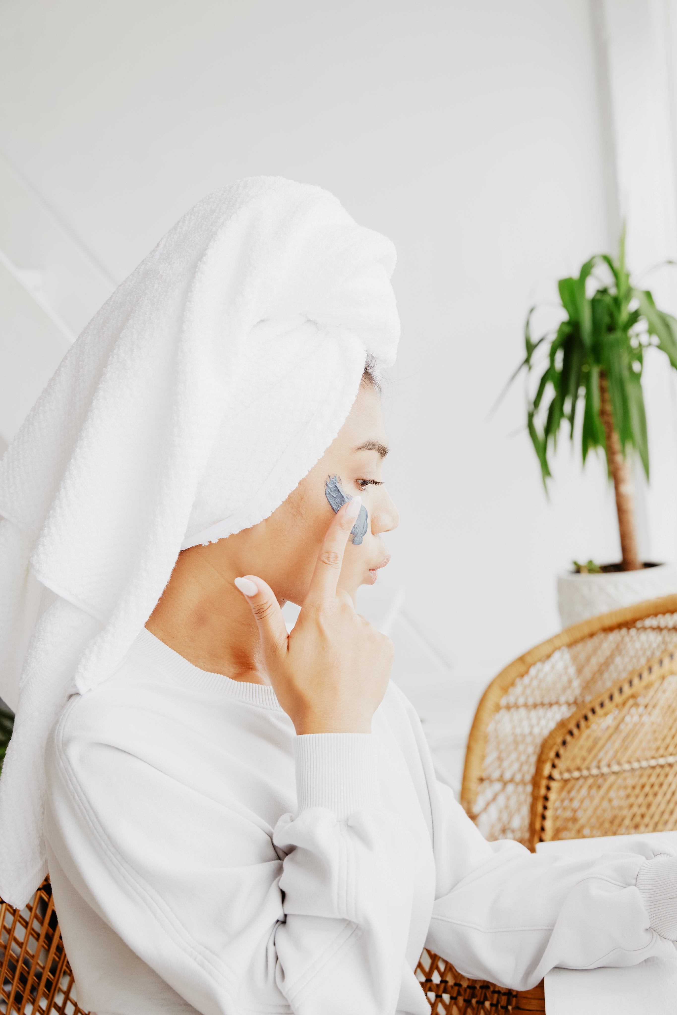 A woman wearing a white towel applying facial moisturizer. 